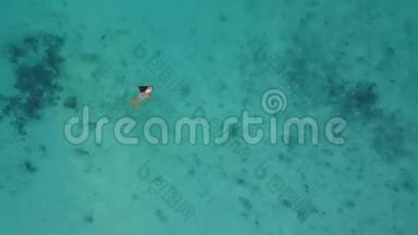 空中摄像机在一个迷人的女子身上升起，她穿着比基尼，<strong>漂浮</strong>在环礁热带岛屿晶莹剔透的<strong>海面</strong>上